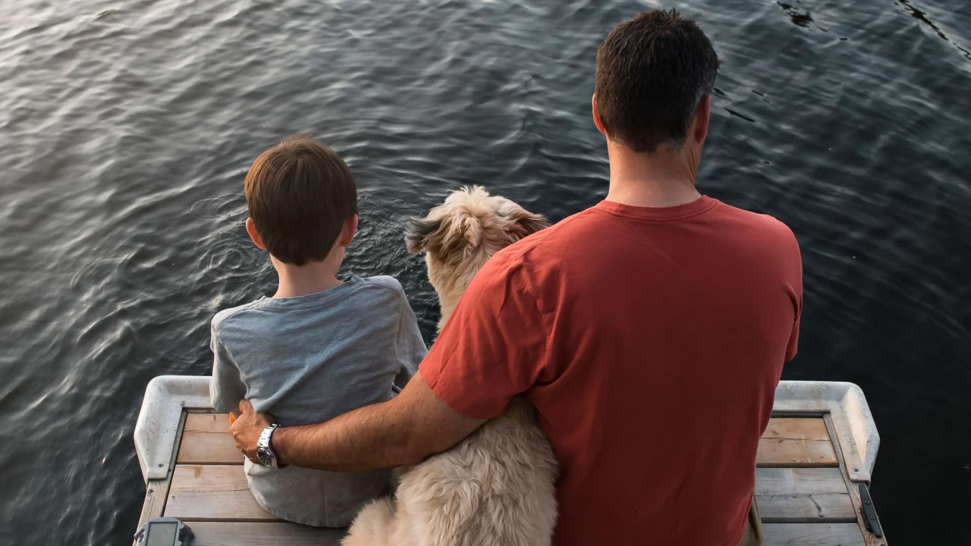 Vater, Sohn und Hund sitzen am Steg und blicken auf den See