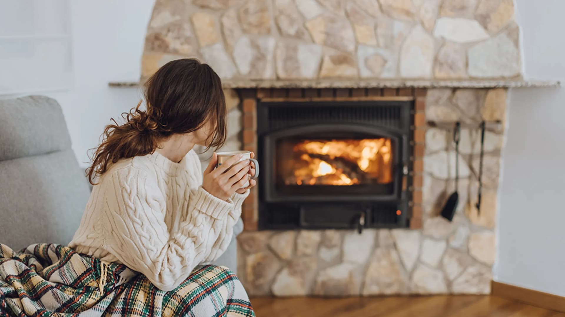 Frau mit Tasse vor einem Kaminofen mit Feuer