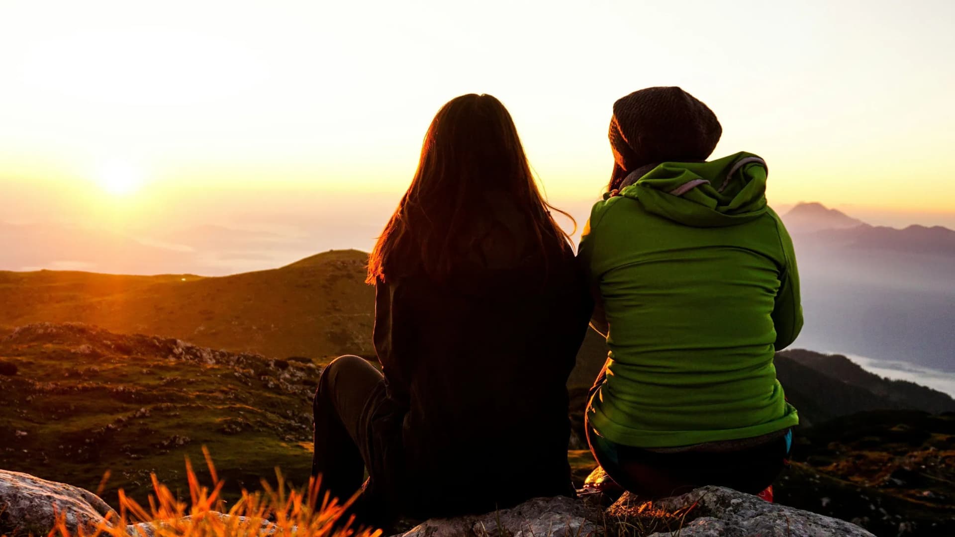 Freunde sitzen auf einem Berg im Sonnenuntergang als Symbolbild für "Gute Freunde sind uns was wert - unsere Freundewerbung zahlt sich aus!"